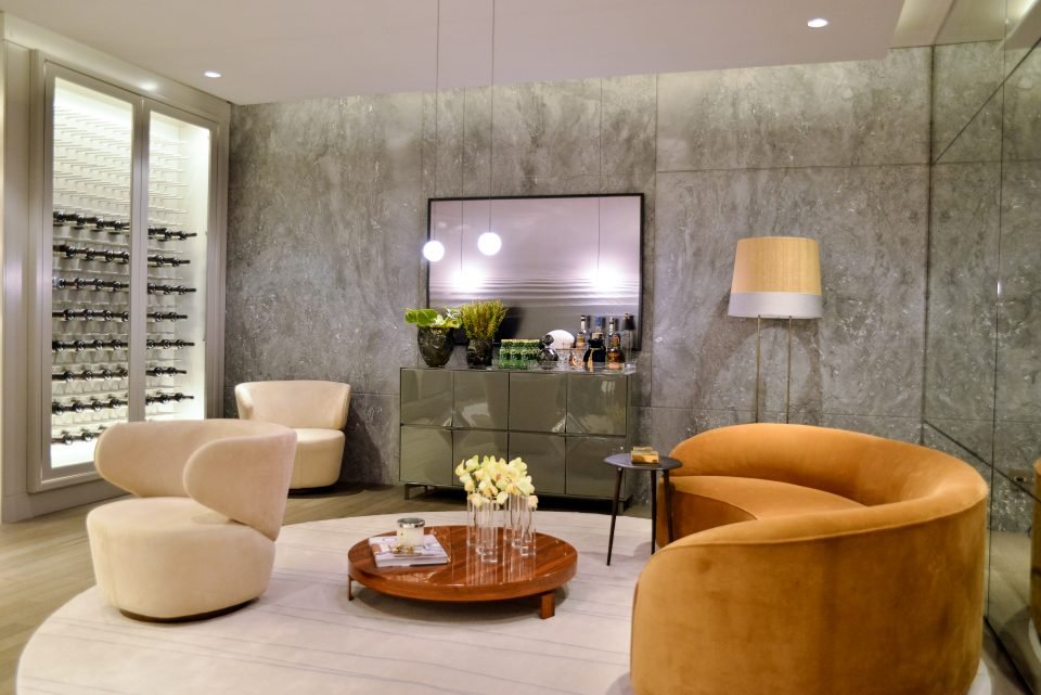 A interação entre o Home Theater e o espaço de degustação de vinhos emerge do conceito contemporâneo pela arquiteta Ana Carolina Gori. A adega com portas de vidro Cebrace Extra Clear e com iluminação de destaque branca criou um canto luminoso e de charme para guardar os vinhos.